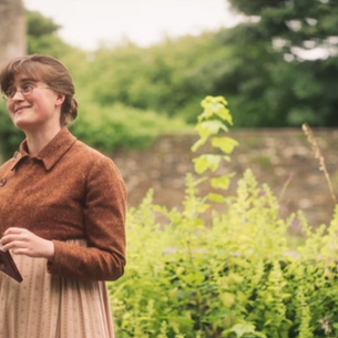 A young woman holds a book and smiles in a garden
