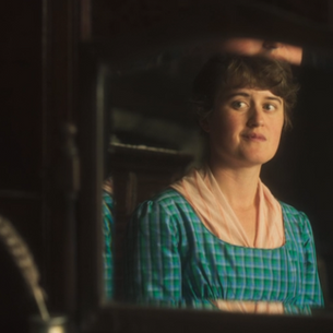 A young woman in a blue dress looks at herself in the mirror and smiles