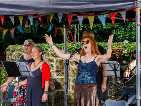 woman holding her arms up singing leading the rest of the band members under a gazebo at a music festival