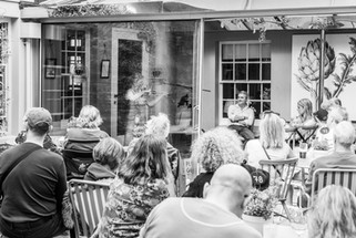 audience sitting in courtyard watching artistically dapled violinist behind a glass partition