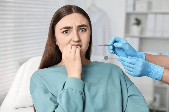 A young female patient is covering her mouth with her hand at the dentist. She is feeling nervous