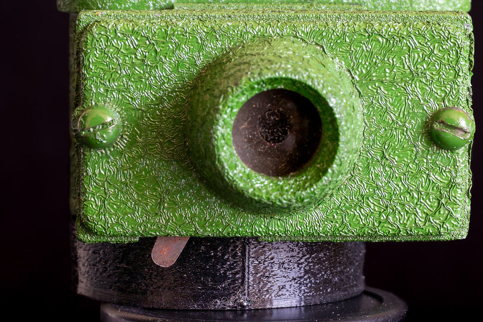 Close-up of a textured green metal object with a round protrusion, two screws, and a black base against a dark background.