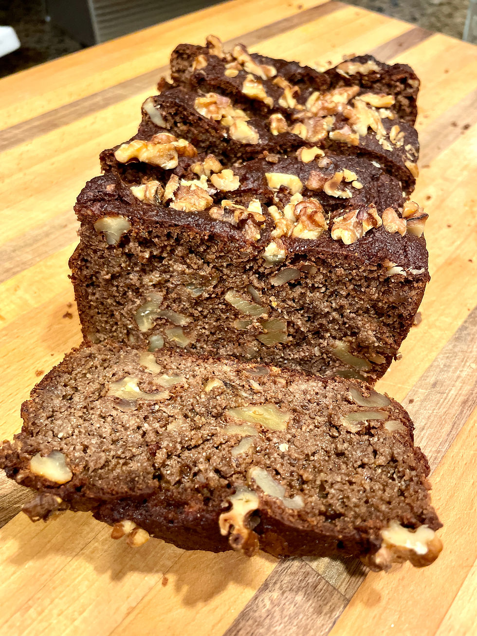 Sliced loaf of chocolate cake with walnuts on a wooden board, displaying a rich brown color with nut pieces on top, creating a warm and inviting look.