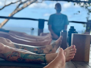 A man sits in the background as he guides students from a yoga class.