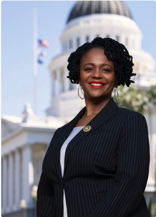 African American woman wearing white blouse and black blazer standing in front CA capitol building.