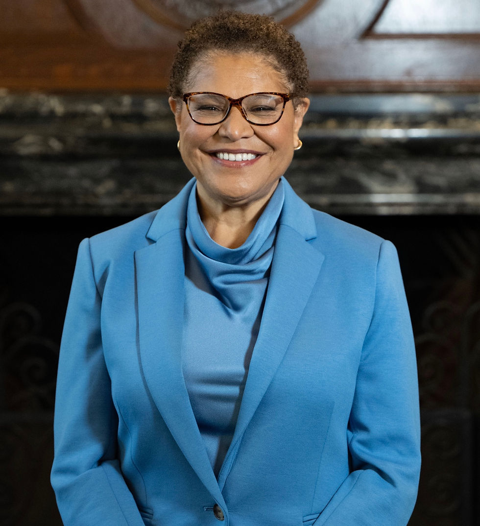 African American woman standing in Mayor's office, wearing light blue suit, short hair and tortoise shell frame eyeglasses.