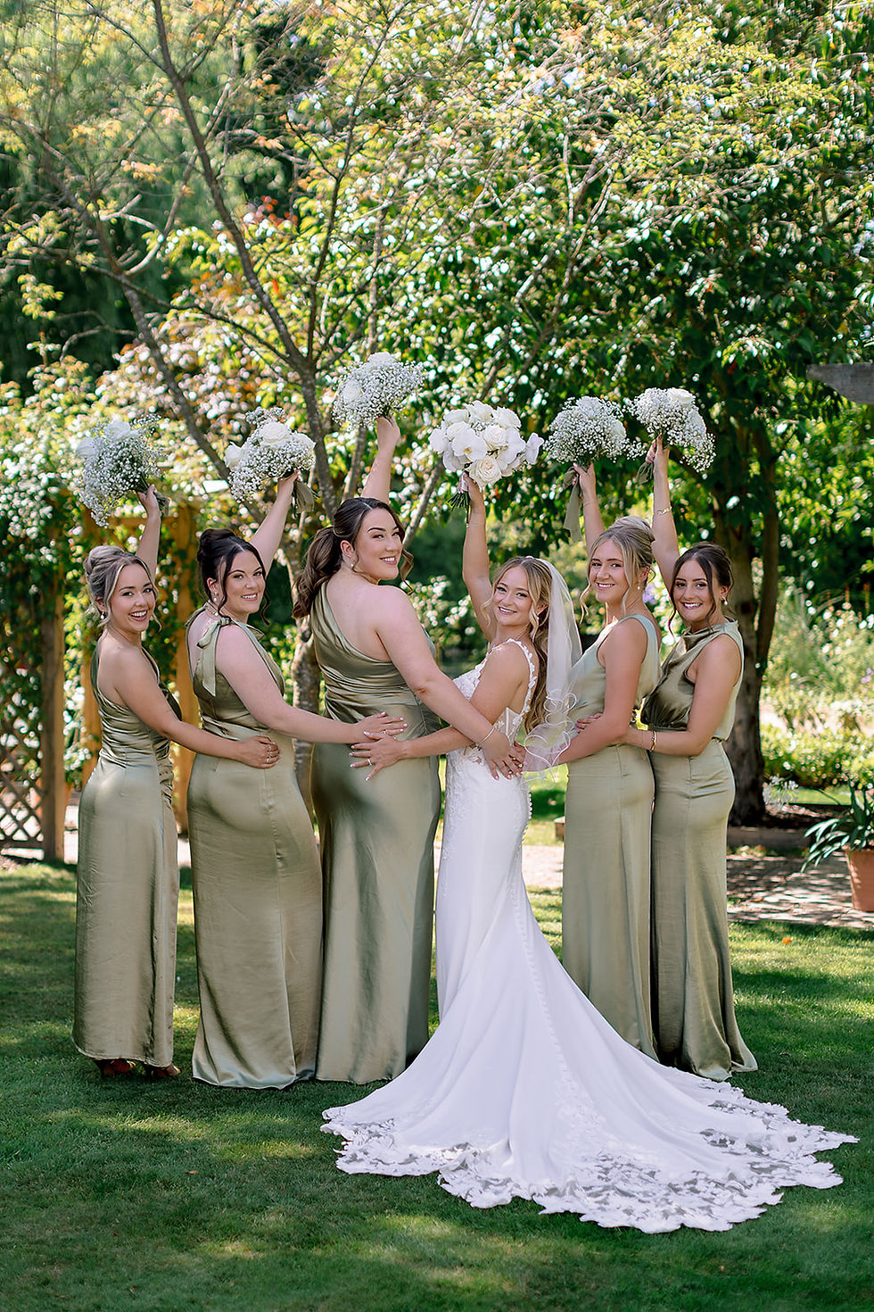 A bride and her bridesmaids turn to face the camera and hold their bouquets in the air.
