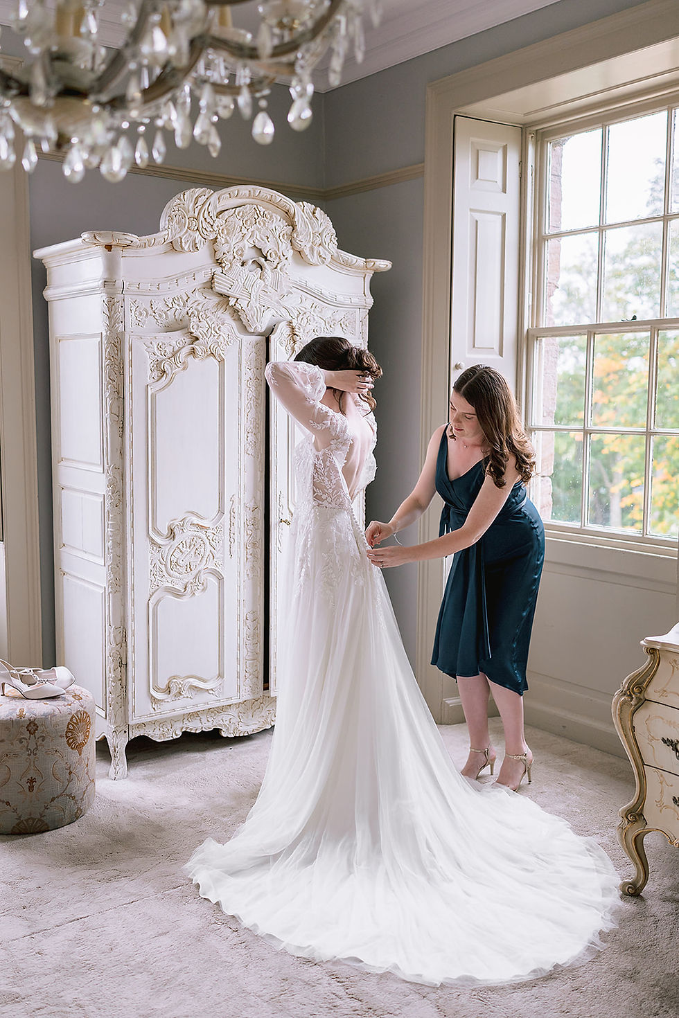 bridesmaid in dark green fastening a brides white wedding dress at Newton Hall
