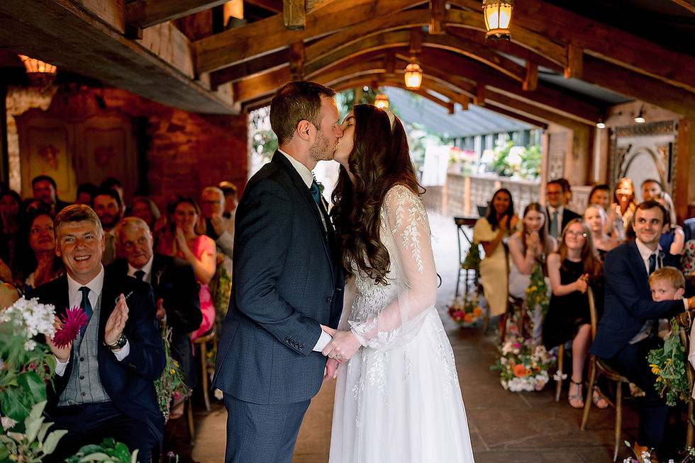 A couple kiss during their wedding ceremony in a chapel surrounded by red white and pink flowers