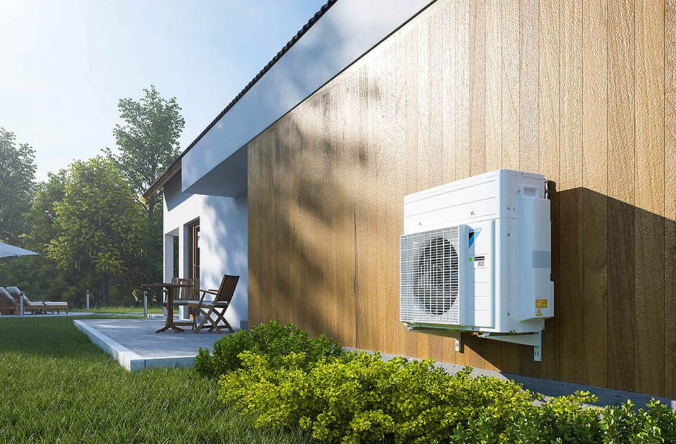 Air conditioner on a wooden house wall, patio with chairs and umbrella in the background, lush green lawn and bushes, sunny day.