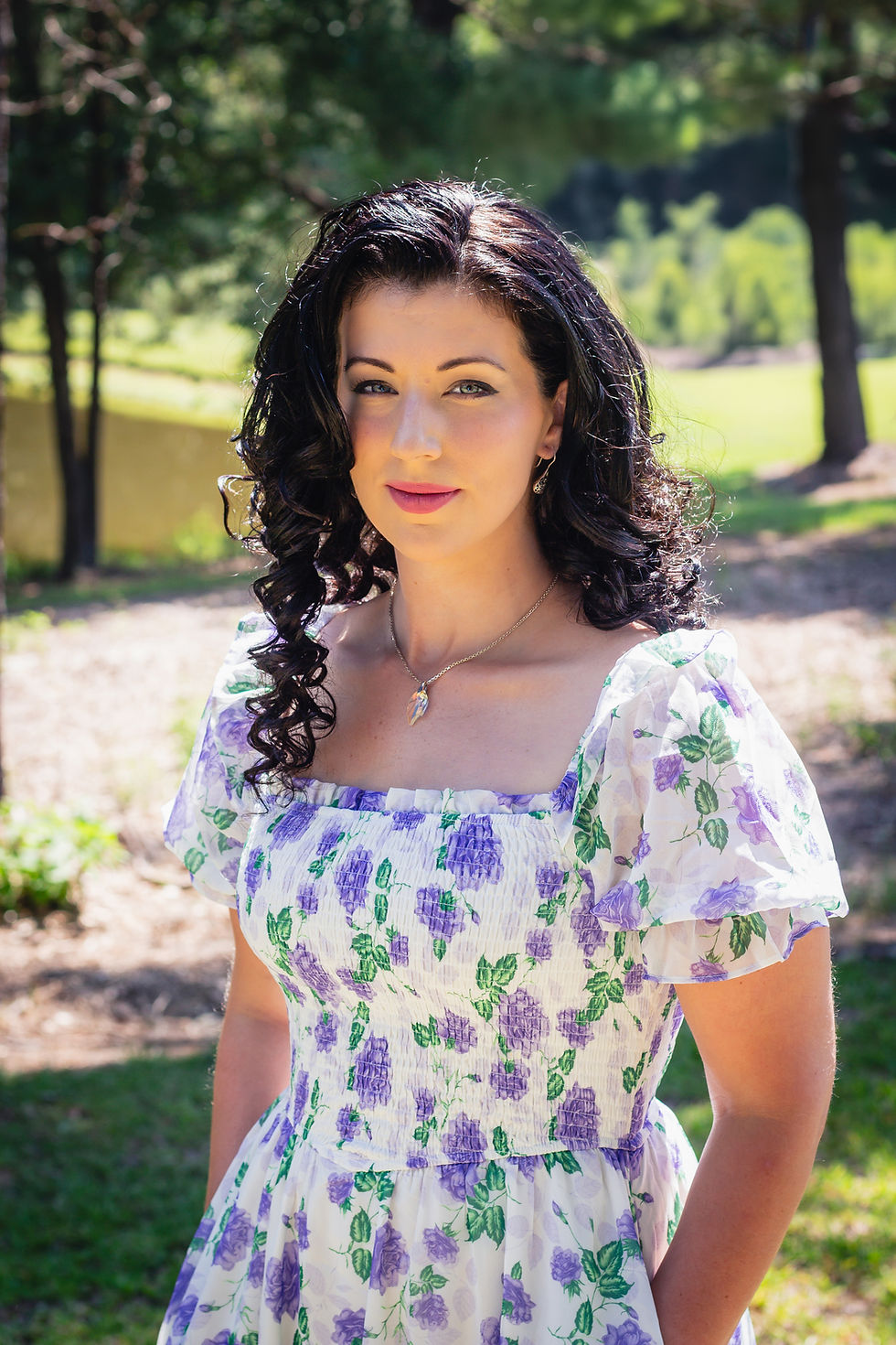 Photo of author with dark curly hair and wearing a white and purple dress