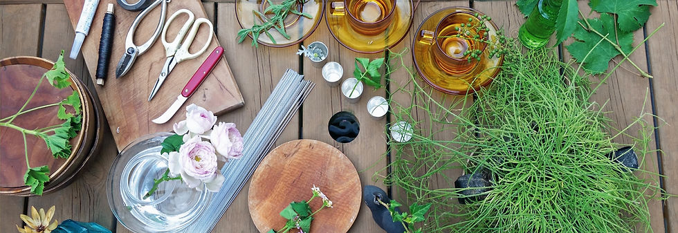 ワイヤー、カップ&ソーサー、植物、花器、フラワーナイフなどがランダムに木の机に並んでいる
