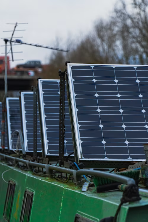 Row of solar panels mounted on a green boat roof, with an overcast sky and blurred trees in the background.