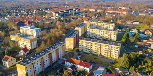 Aerial view of a residential area with colorful buildings, mainly yellow and orange. Cars line the streets, surrounded by greenery and trees.