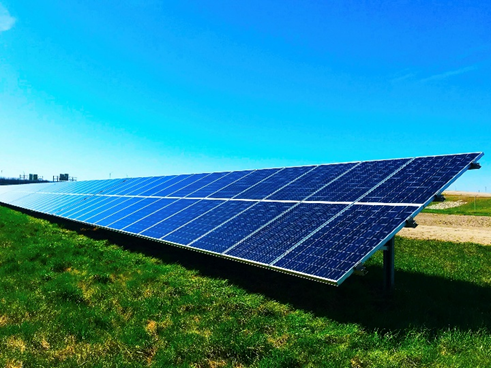 Solar panels on green grass under a clear blue sky. The panels are angled to capture sunlight, symbolizing clean energy and sustainability.