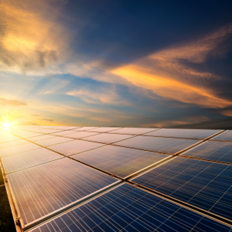 Solar panels stretching into the distance at sunrise under colorful clouds, glowing with warm golden light.