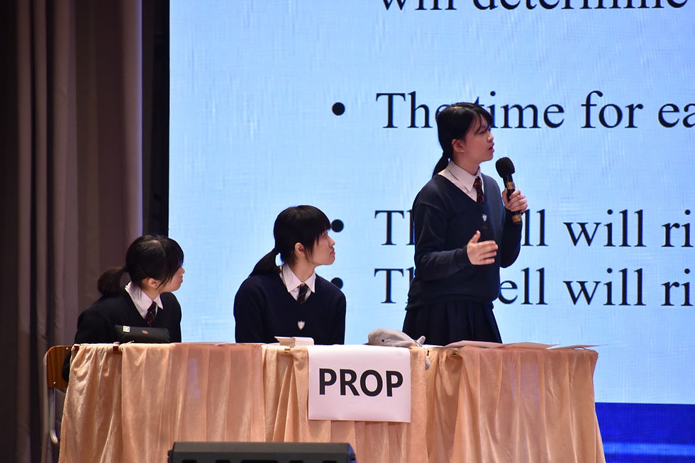 Students in school uniforms debating on stage at a table labeled PROP