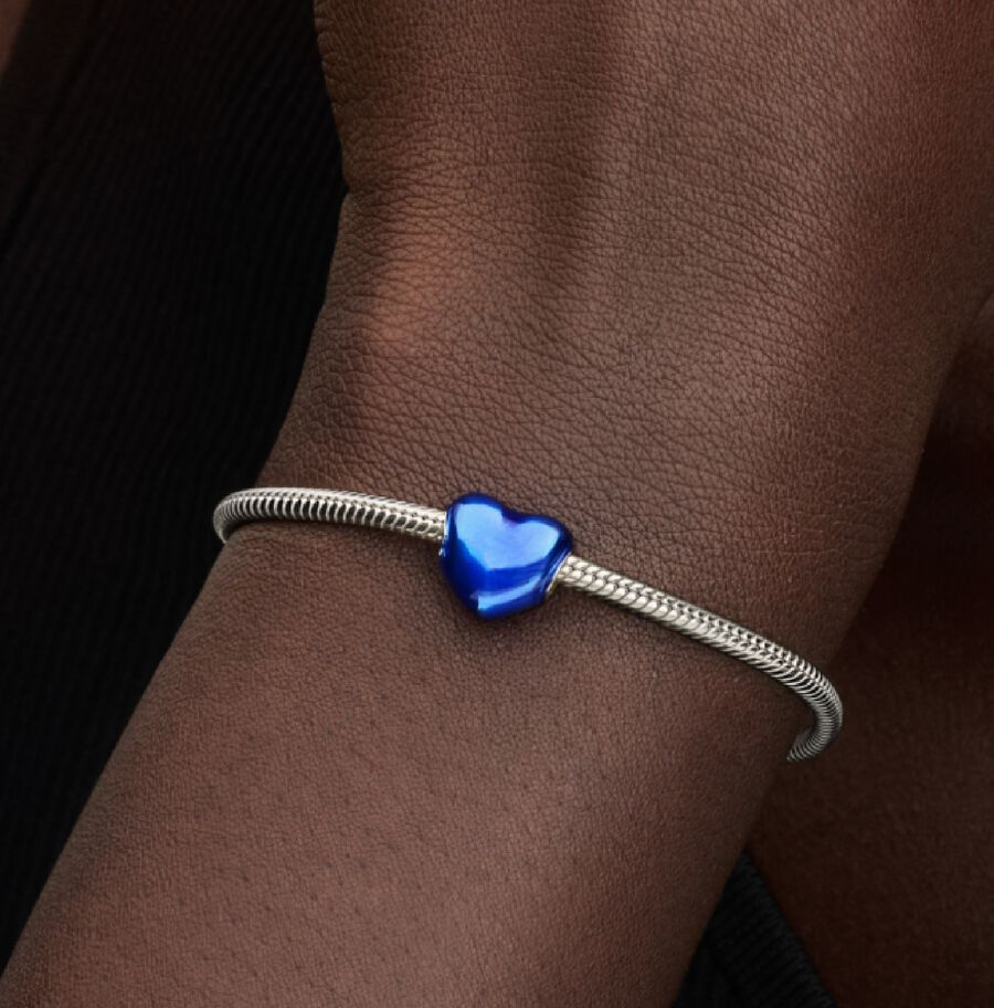Silver bracelet with a blue heart charm against dark skin background.