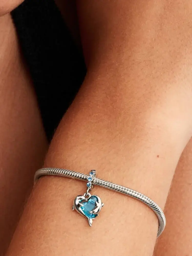 Silver bracelet with blue heart charm on a wrist; Pandora Blue Murano Glass Dolphins Dangle Charm.