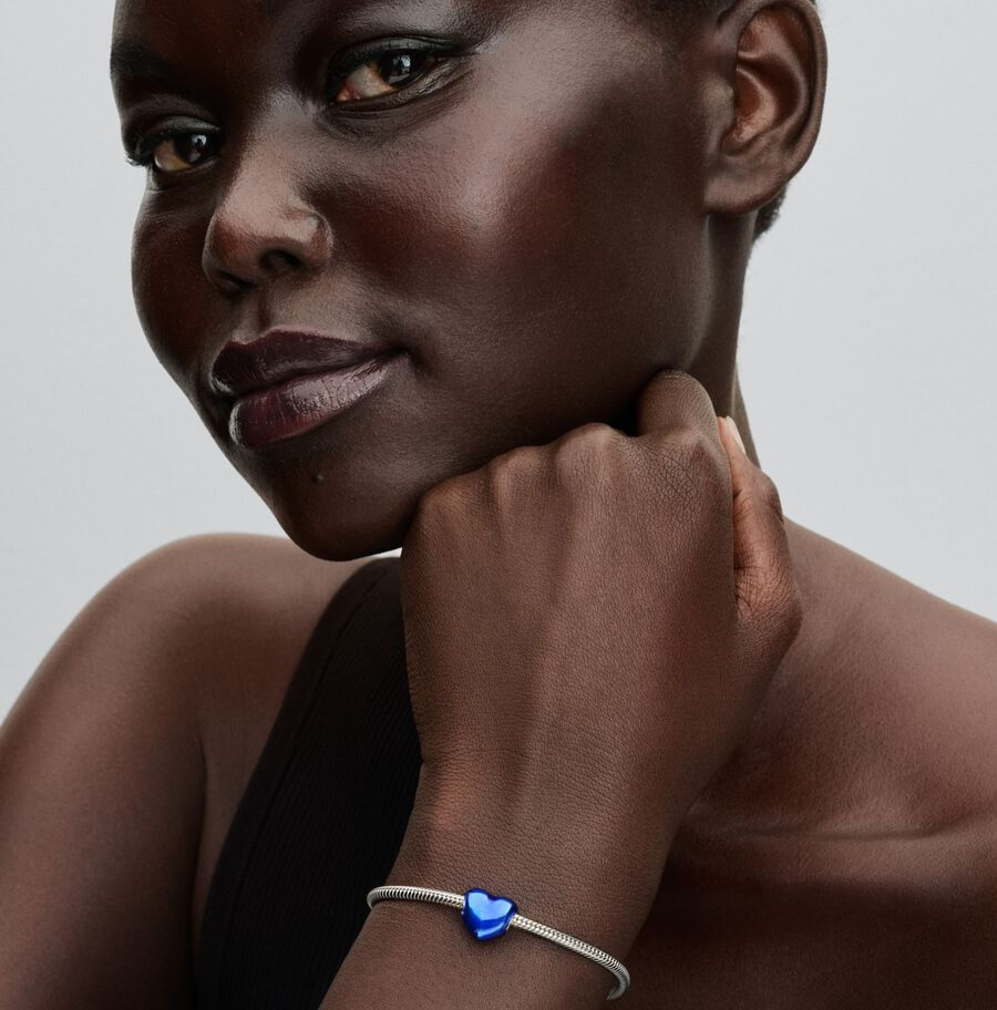 Woman wearing a blue heart charm bracelet, hand on chin, Jewels by the Sea.
