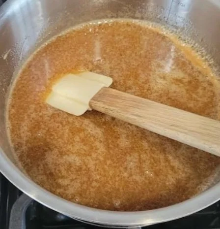 Caramel sauce simmering in a saucepan with a spatula stirring, made without butter or dairy.