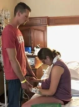 Woman in hospital labor room leaning forward during labor while husband supports her hands.