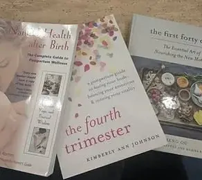 Three postpartum books laid on a table: Natural Health After Birth, The Fourth Trimester by Kimberly Ann Johnson, and The First Forty Days.