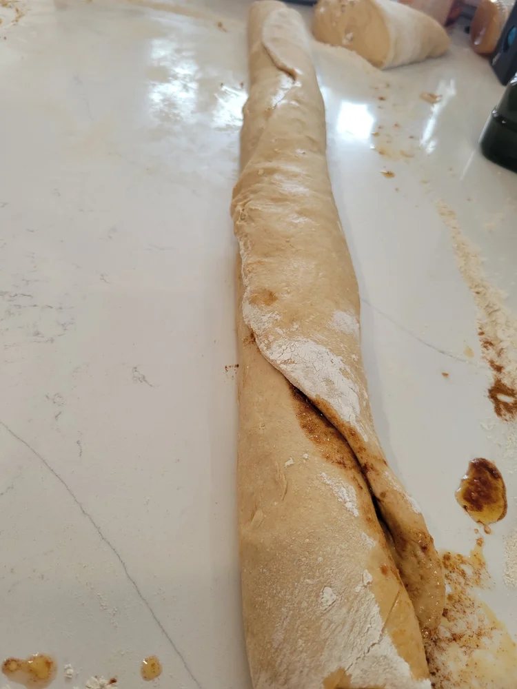 Rolled cinnamon roll dough log ready to slice before baking.