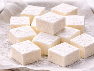 Freshly cut homemade marshmallows dusted with arrowroot powder, arranged on parchment paper in soft square shapes, highlighting their fluffy texture and clean ingredients.