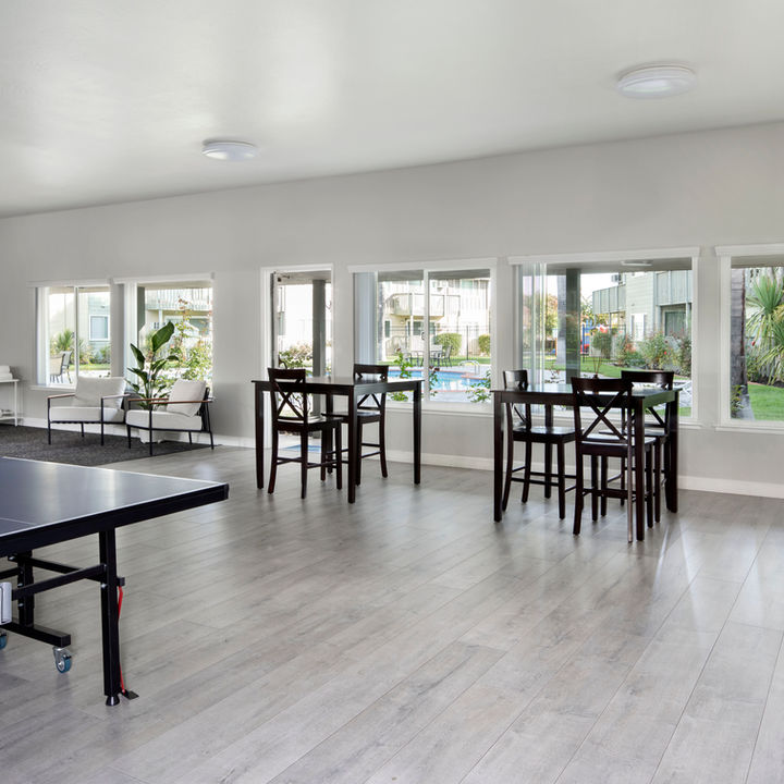 A spacious recreation room with a ping pong table, several high-top tables, and a kitchenette area with a fridge on the right.