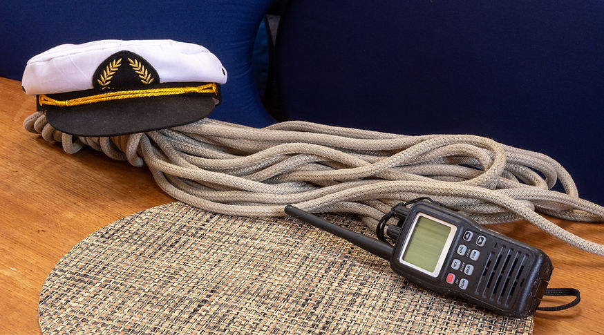 A handheld VHF marine radio and captain's hat with a rope on a boat table.jpg