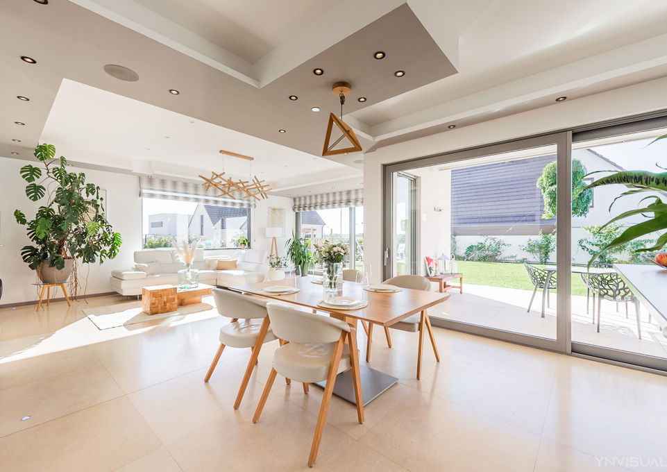 Salle à manger panoramique entourée de plantes, éclairée par des spots, avec vue sur jardin extérieur par baie vitrée