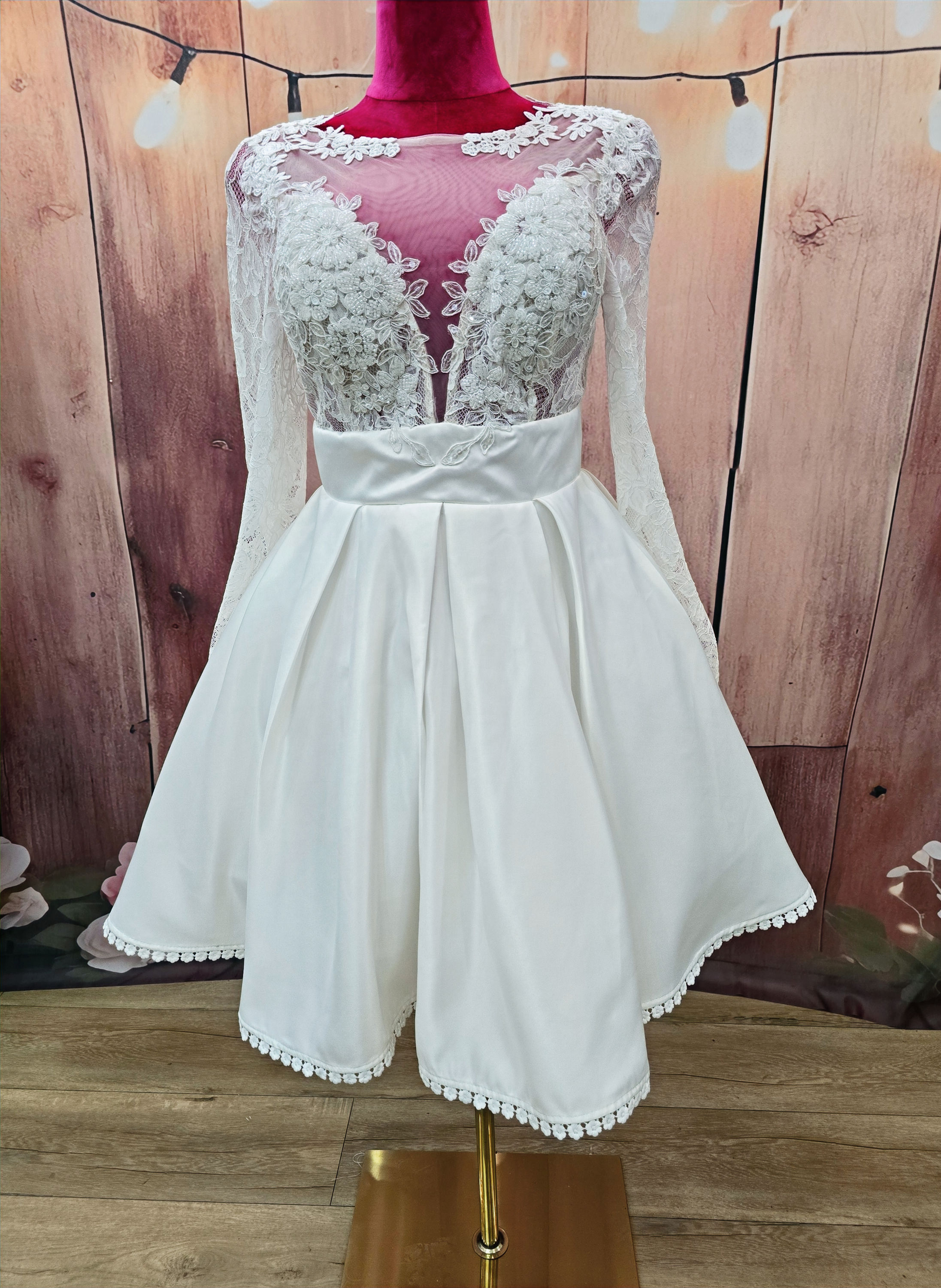 Vestido de novia corto modelo Xanthe con escote ilusión en tul bordado, mangas largas de encaje y falda satinada con cinturilla marcada. Diseño sofisticado y elegante para novias modernas.