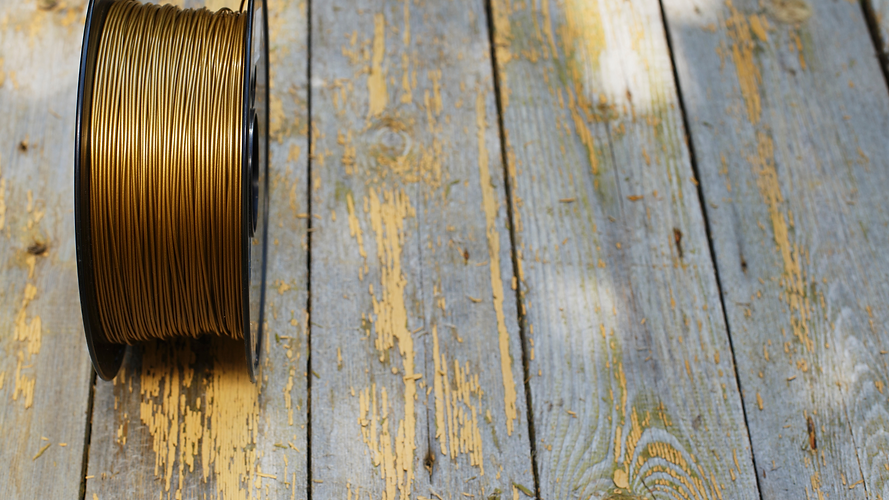 Bobine de filament 3D bronze sur planches de bois usées.