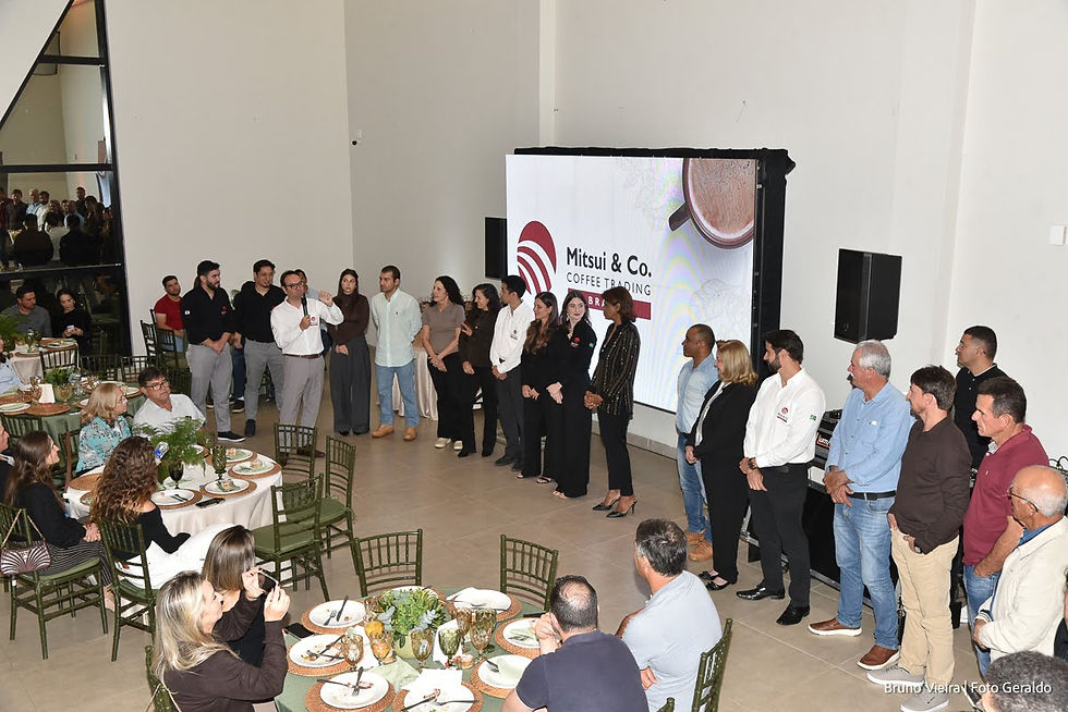 Grupo em evento corporativo em salão elegante; pessoas alinhadas ao lado de tela com Mitsui & Co. Coffee Trading.