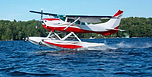 A red and white Cessna 206 water plane landing on a lake.