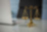 Golden scales of justice on a reflective desk beside a partially open laptop, set in a professional office environment.