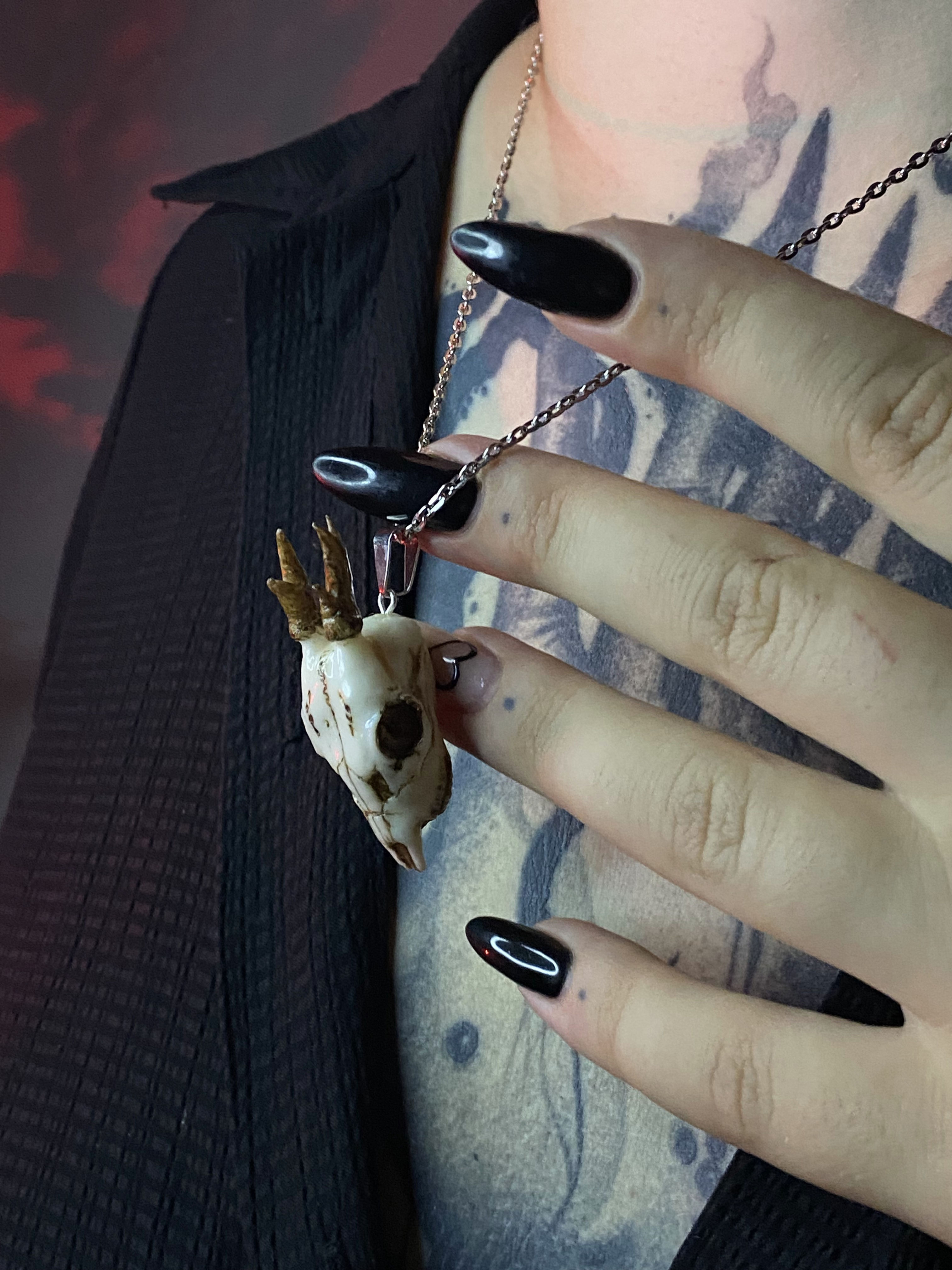 Дівчина з тату на грудях вдягає кулон у вигляді черепа оленя.