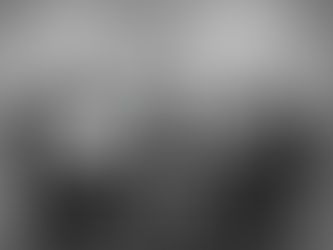 Two people wearing headphones sit at a table with microphones, engaged in conversation. The setting is a simple, gray studio.