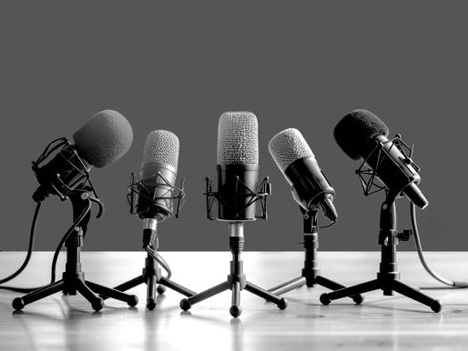 Six black and gray microphones on stands are arranged on a reflective wooden surface against a plain gray background, creating a professional vibe.