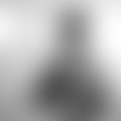 Man in white shirt examines camera, focused expression. Neutral background with spotlights. Black and white image.