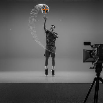 Man in athletic wear jumps, reaching for a glowing ball with a digital trail. Black and gray studio with a camera filming. Modern, dynamic scene.