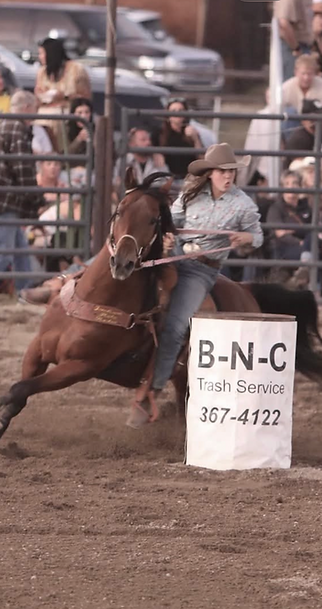 A female barrel racer and her horse take a turn around a barrel