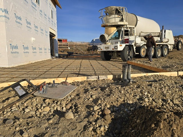 a cement truck pours concrete into a framed up flatwork next to a newly constructed home