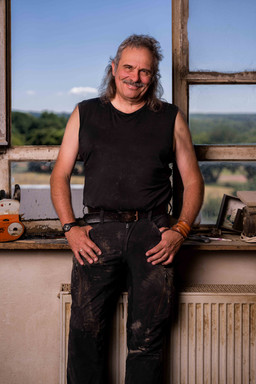 Authentisches Künstler-Portrait von Stephan Guber: Ein ruhiger Moment vor seinen Holzskulpturen bei natürlichem Licht.