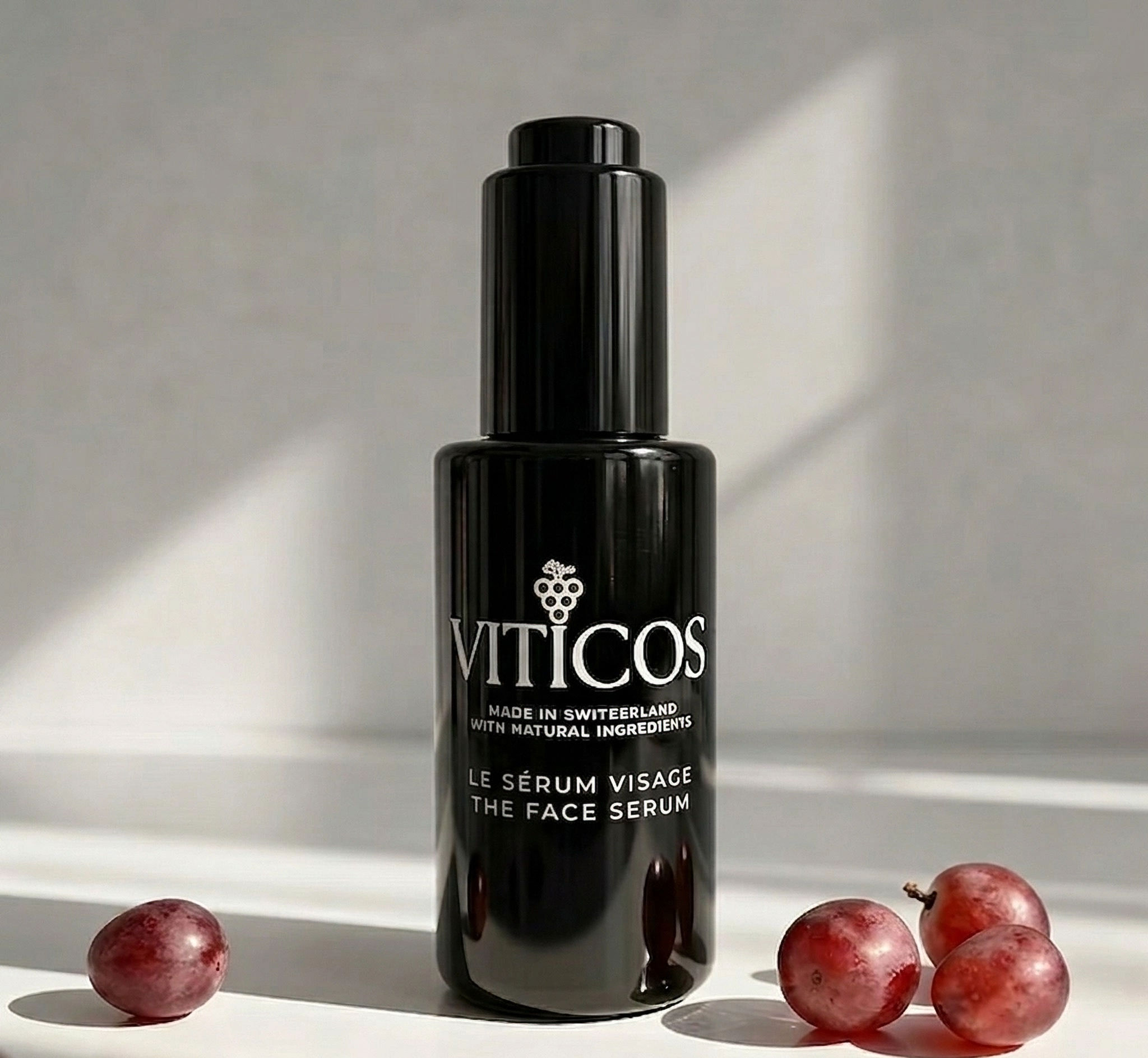 Flacon de sérum visage Viticos entouré de raisins rouges.