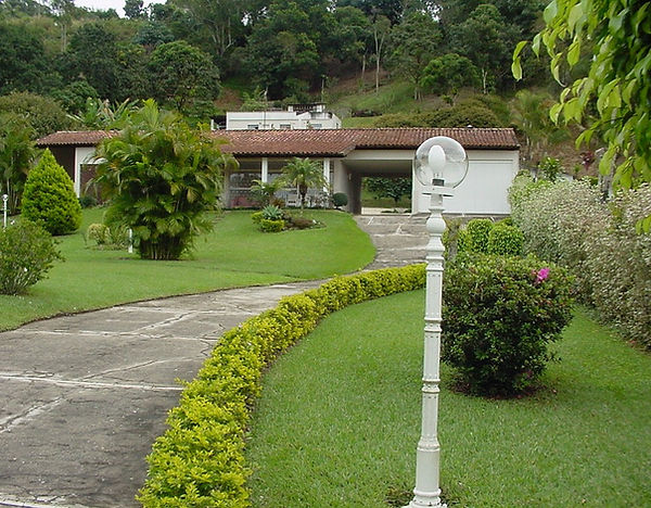 Rampa de acesso à casa, cercada por jardins, vista a partir da entrada da propriedade.