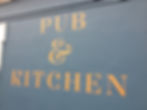 Orange roman lettering on a blue wall saying pub and kitchen