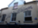 Brown script lettering which says The Wildman, hand painted on a creme wall over the front of the building.