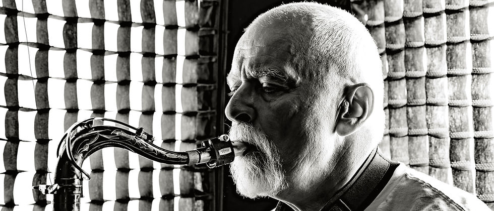 Black and white close-up of a man playing a saxophone. Sunlit grid pattern in the background creates contrast. Text reads "Versa." Mood is intense.
